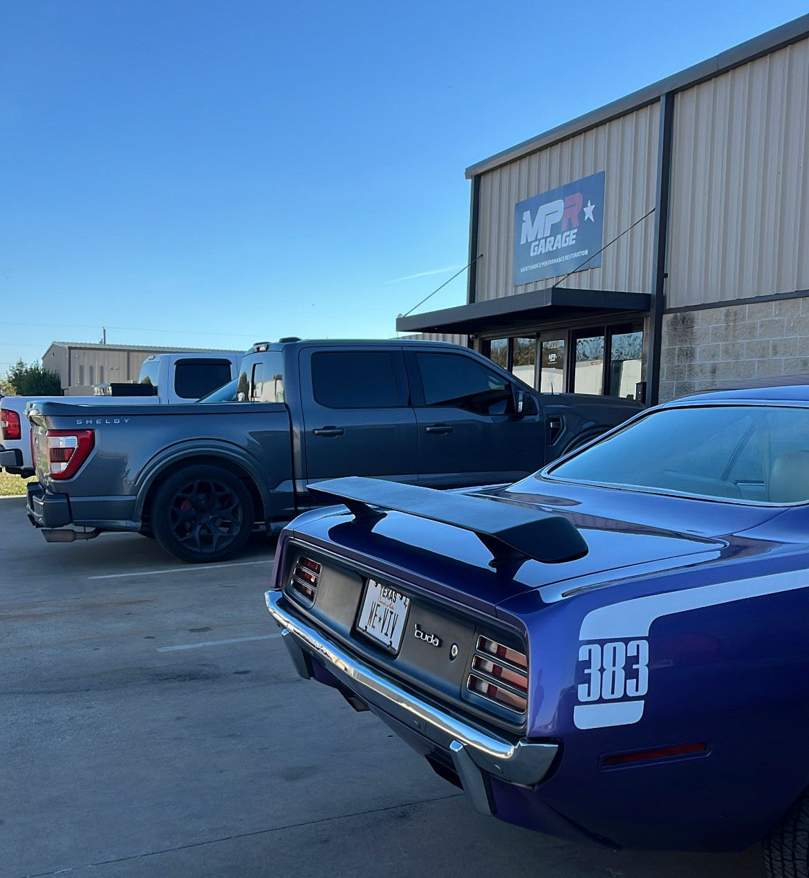 Blue muscle car with a spoiler in a parking lot with a building in the background